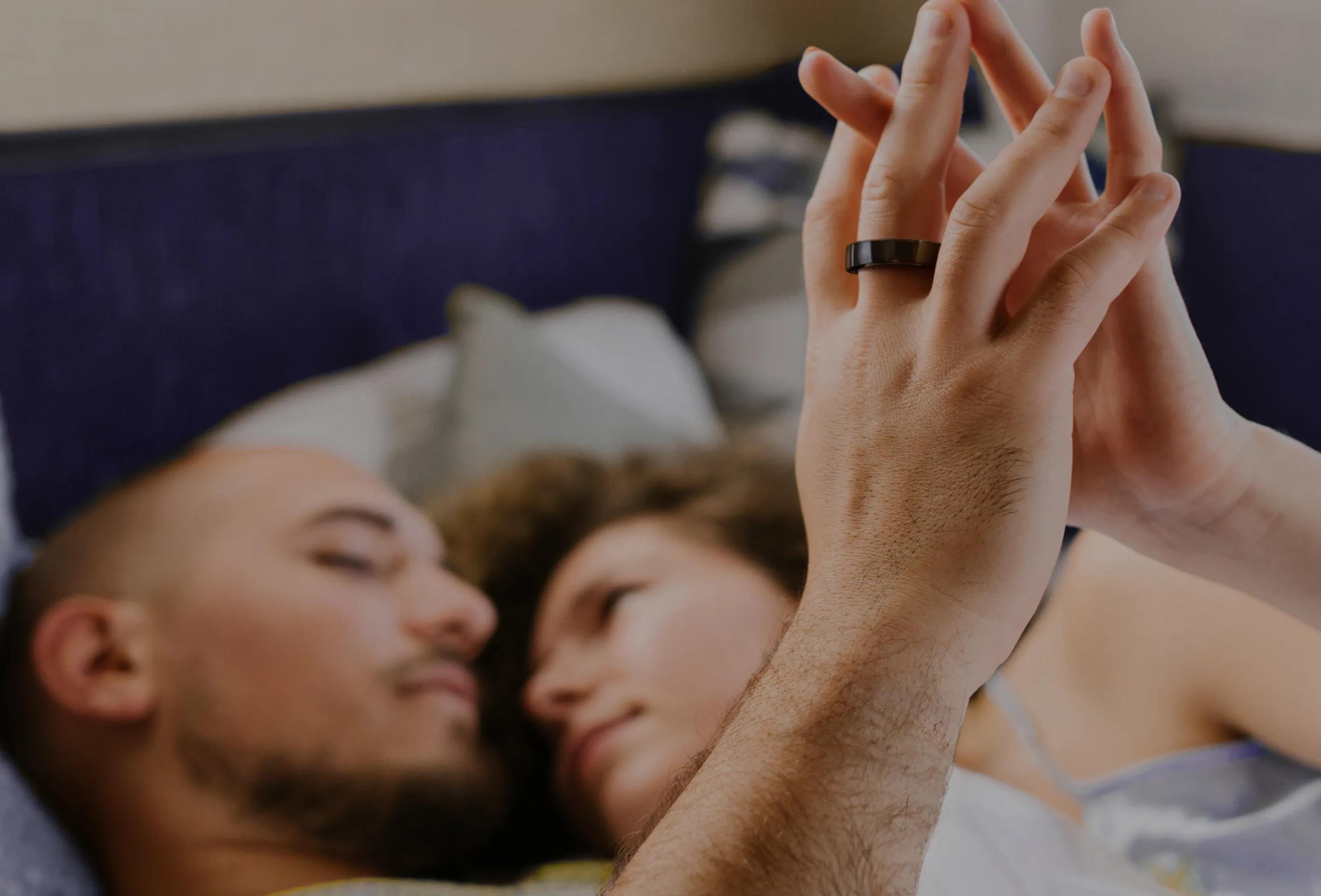 A couple in bed with the black Happy Ring worn on an index finger