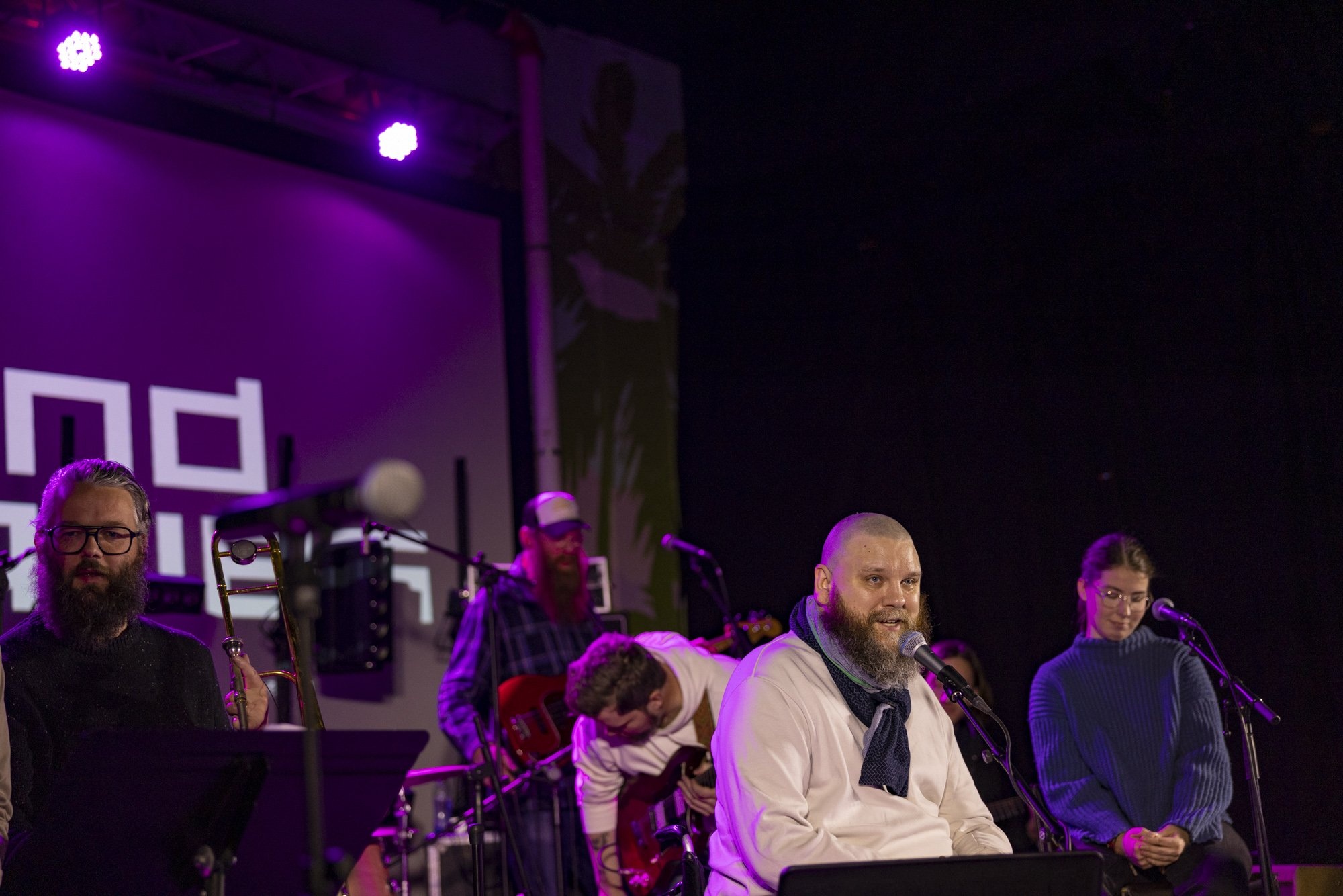 Halli singing at a microphone with fellow musicians on a stage lit in purple.