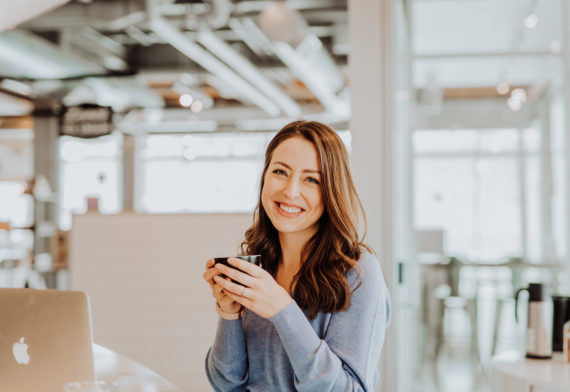 Rachel Mills smiling with a mug beside an open laptop