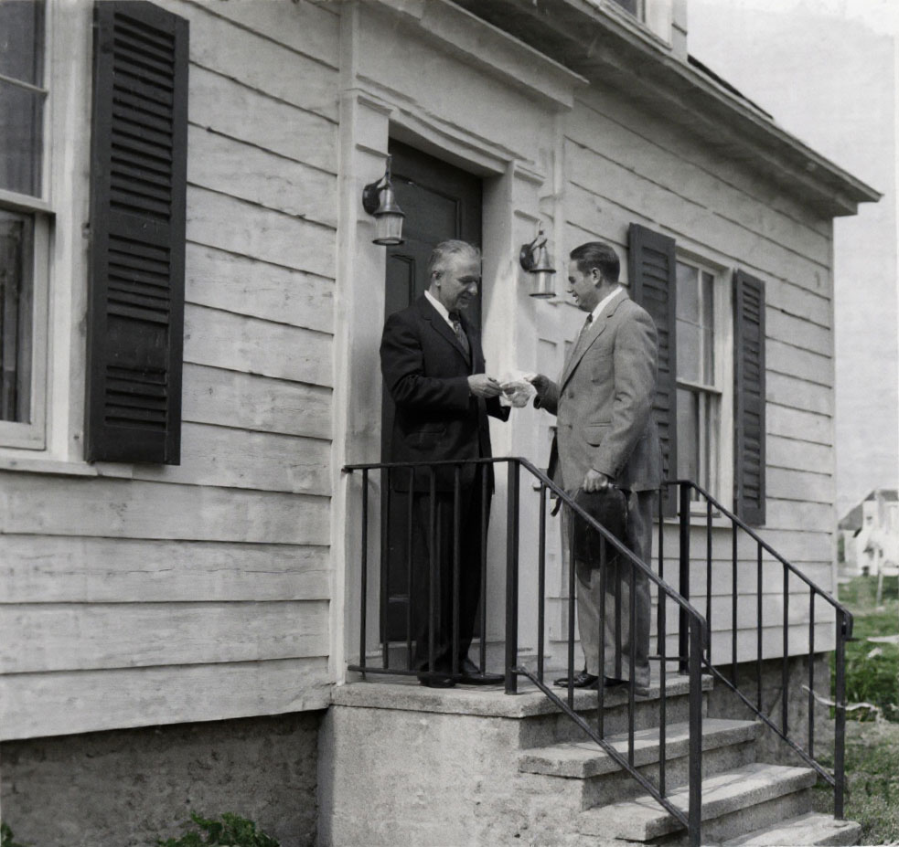 Harold Webster Smith, right, holding his hat while presenting the bank’s first mortgage check to Joe Baltrush on a Waterbury doorstep in December 1935.