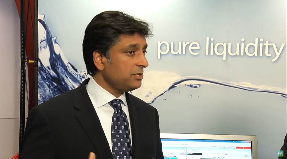 Harpal Sandhu speaking during an interview, with a trading display behind him