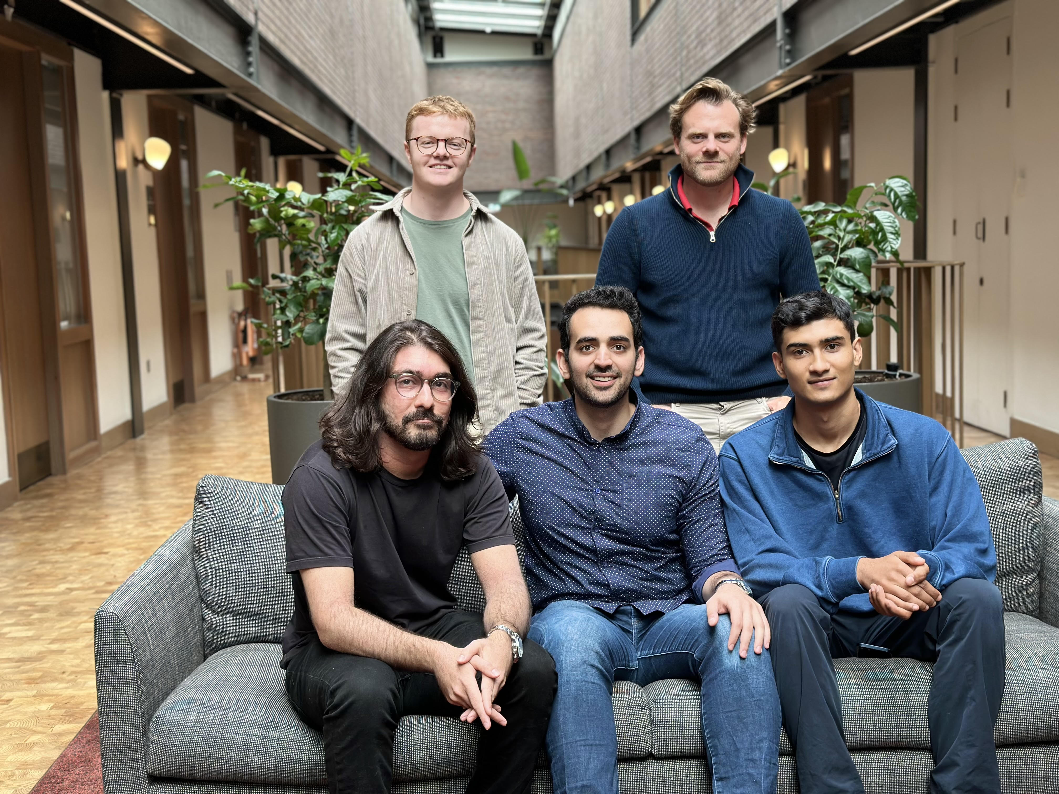 Hasan Sukkar seated in the centre of a sofa with four members of the early 11x team in a bright office atrium