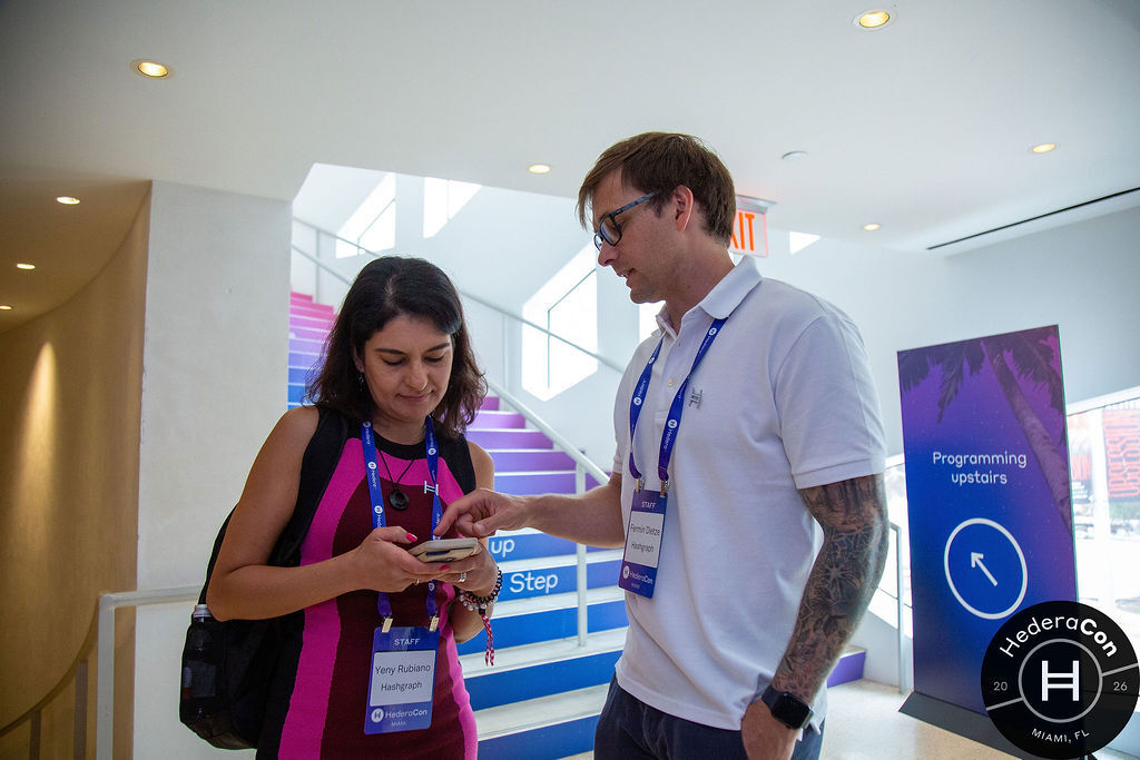 Two Hashgraph staff members comparing a phone screen at HederaCon 2026 in Miami