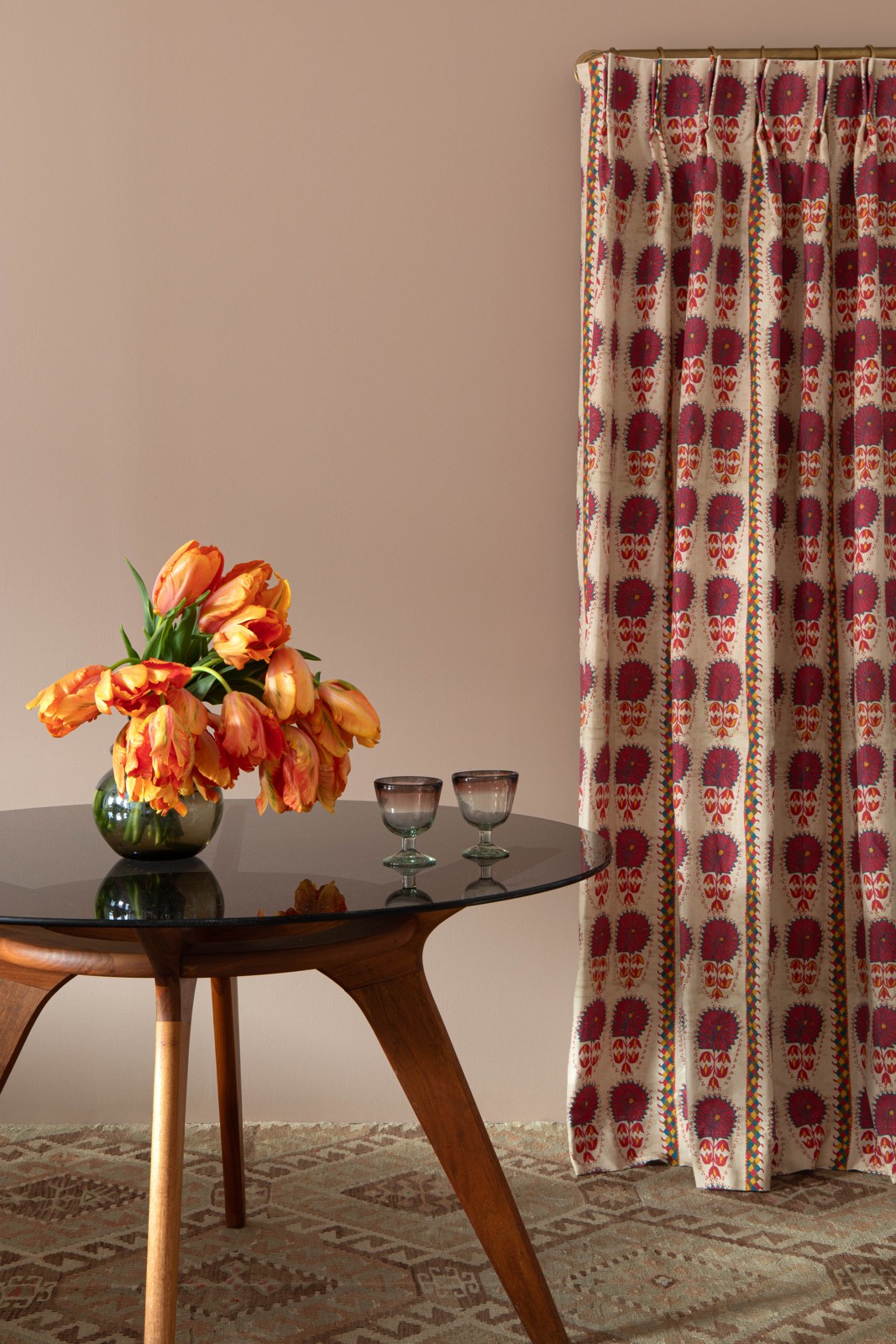 St. Frank patterned curtains beside orange tulips and a glass-topped table