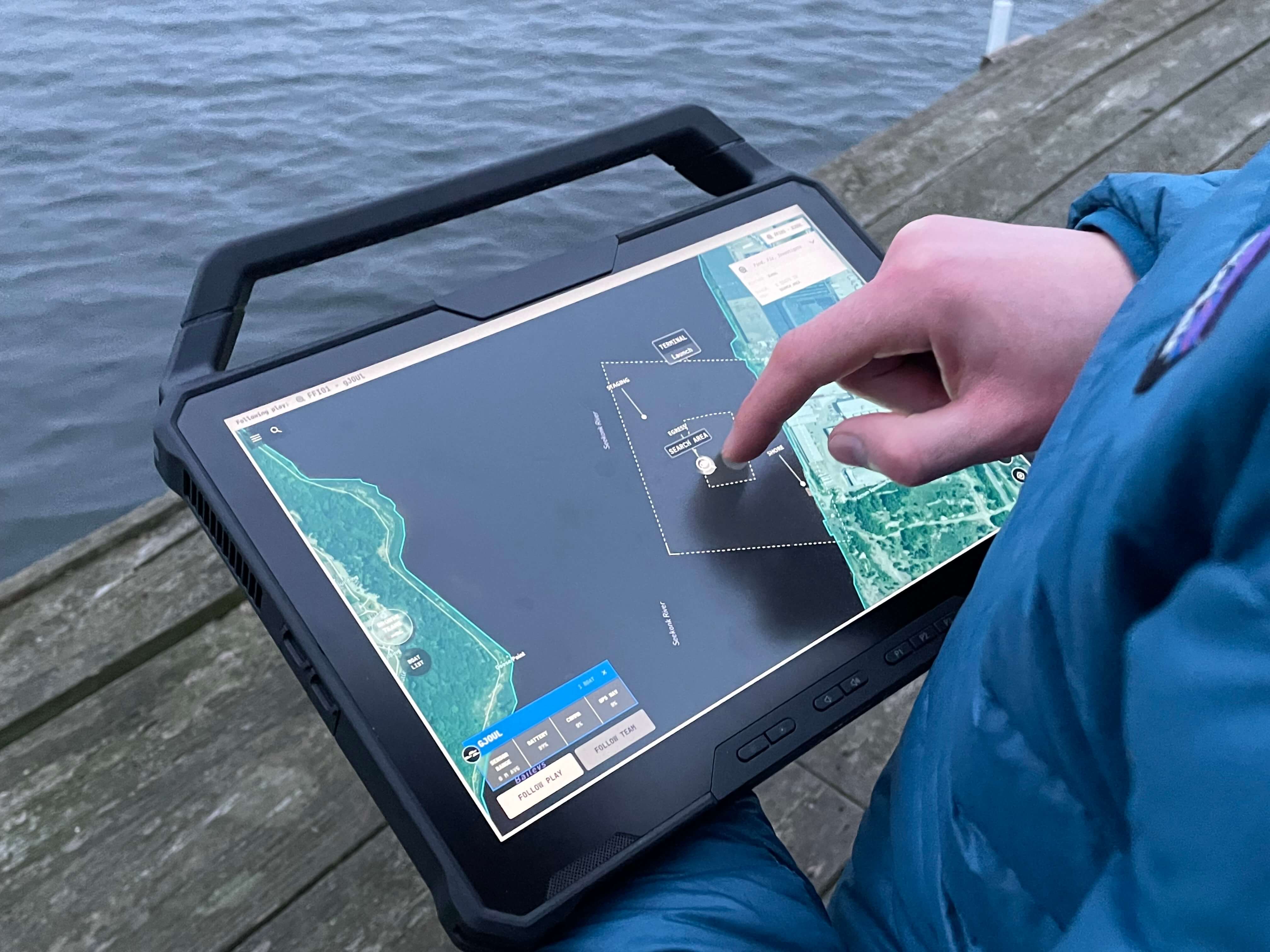 An operator using HavocAI mission planning software on a rugged tablet beside the water