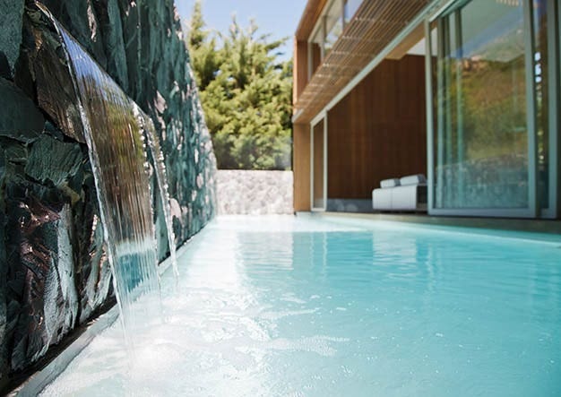 Pool water flowing from a stone water-feature wall beside a modern house