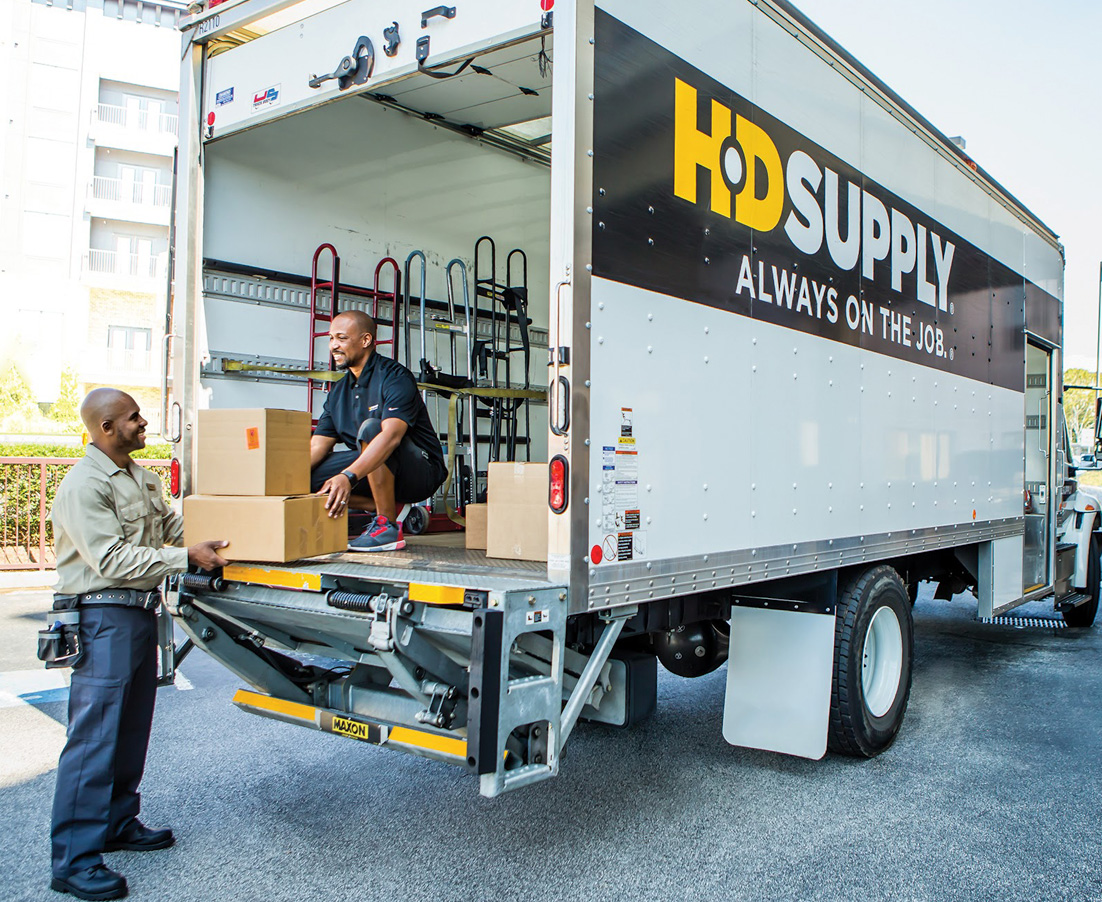 An HD Supply driver hands boxes from a delivery truck to a maintenance professional