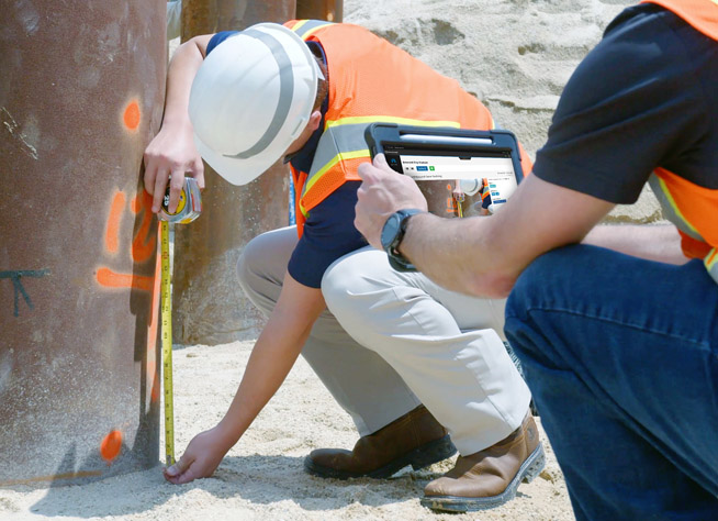 Two construction inspectors measuring a concrete column while using HeadLight on a tablet