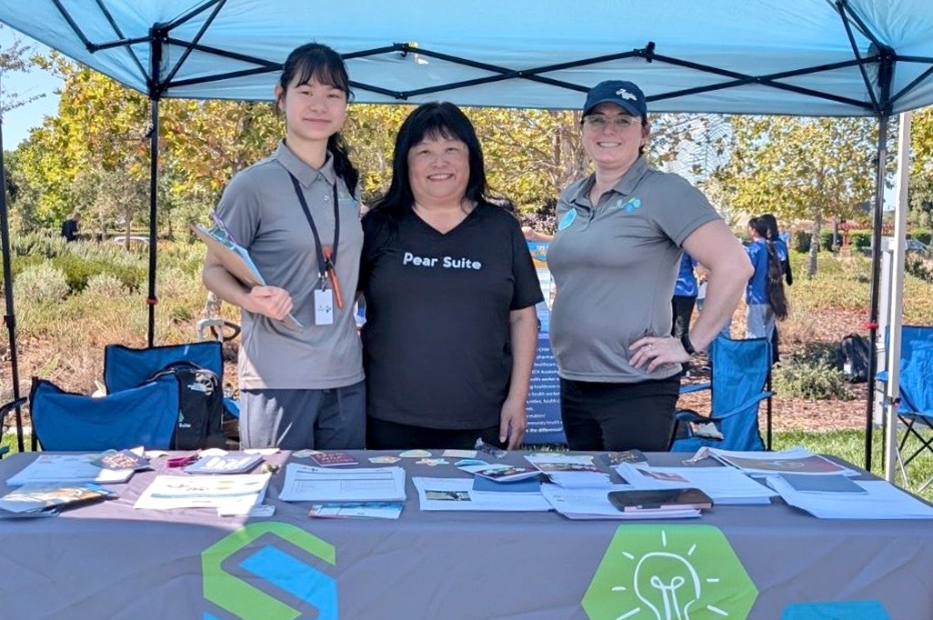 Three people at an outdoor outreach table, including a representative wearing a Pear Suite shirt