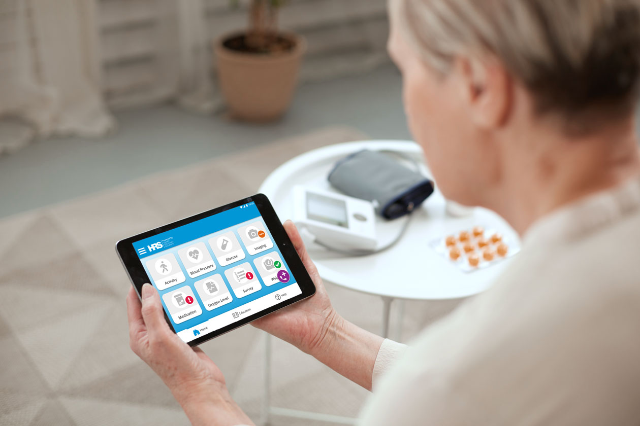 A patient holds an HRS tablet displaying care tools beside a blood pressure monitor.