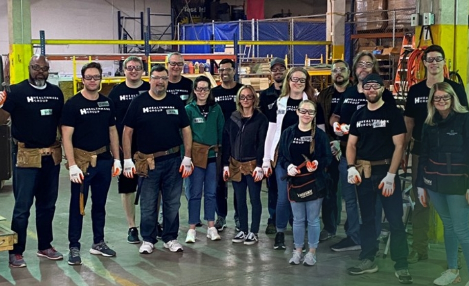 HealthMark employees volunteering together in a warehouse, wearing work gloves and tool belts