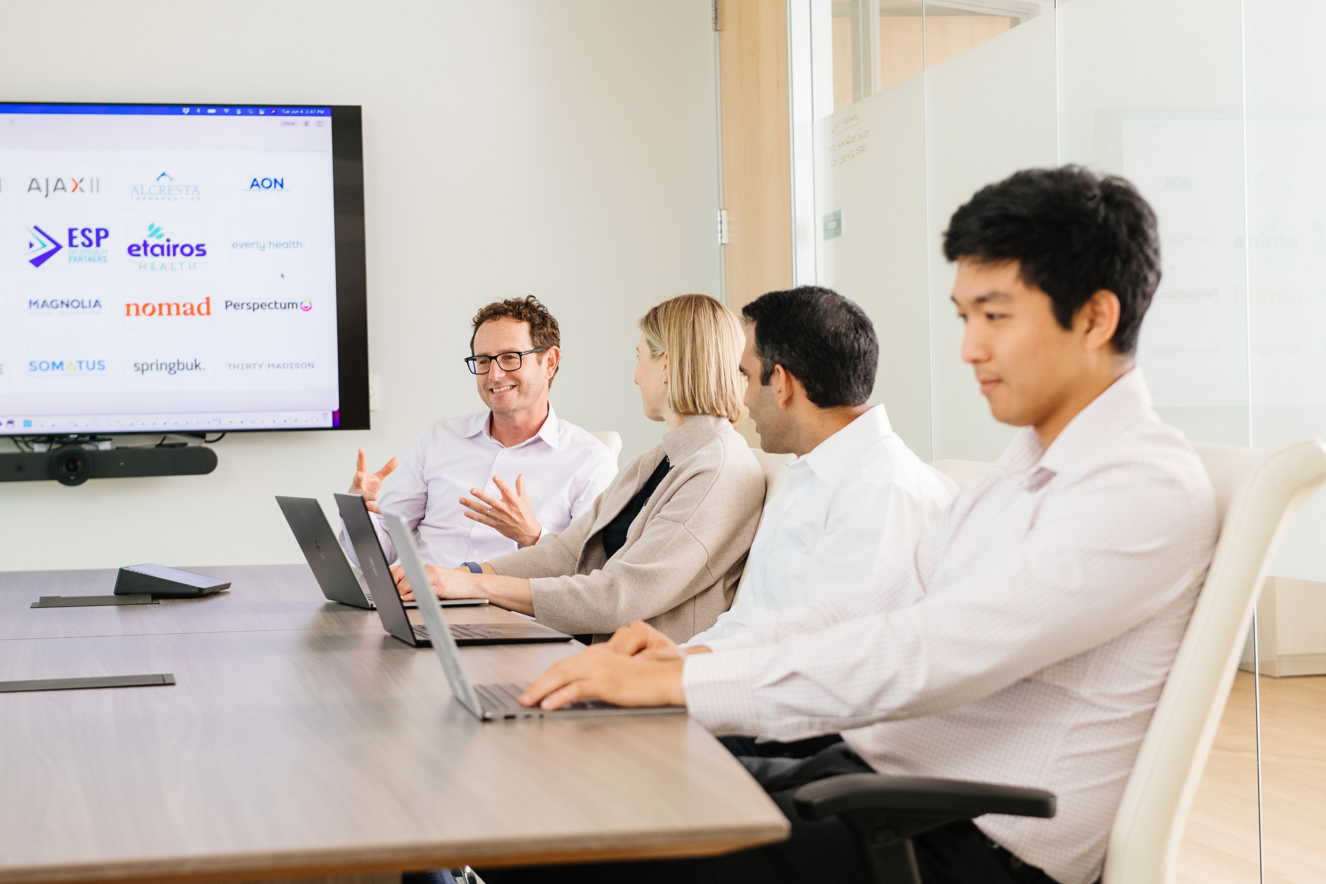 Four HealthQuest team members in a meeting with portfolio company names on a screen