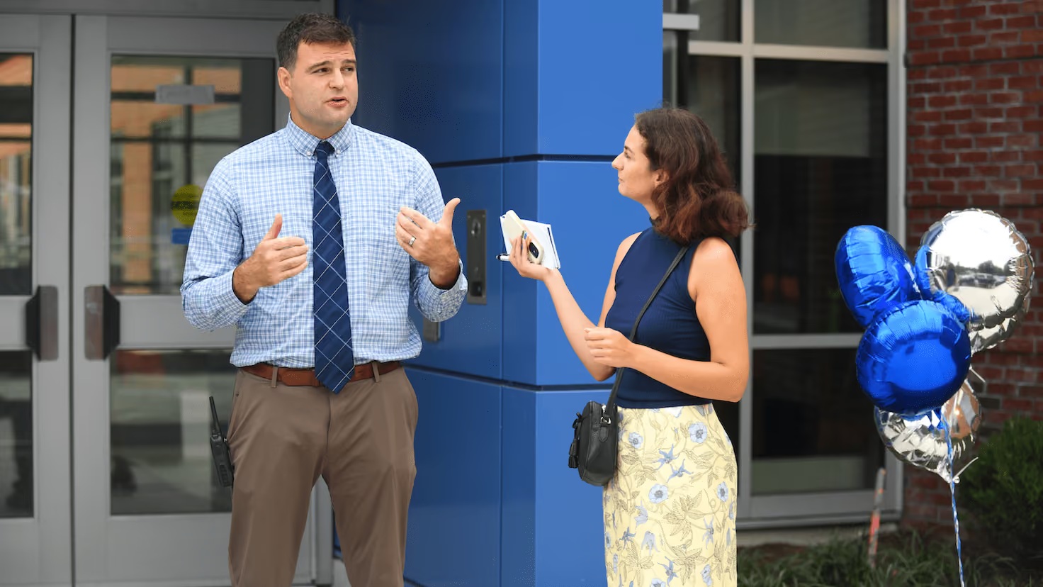 Reporter holding a notepad while speaking with a man outside a building