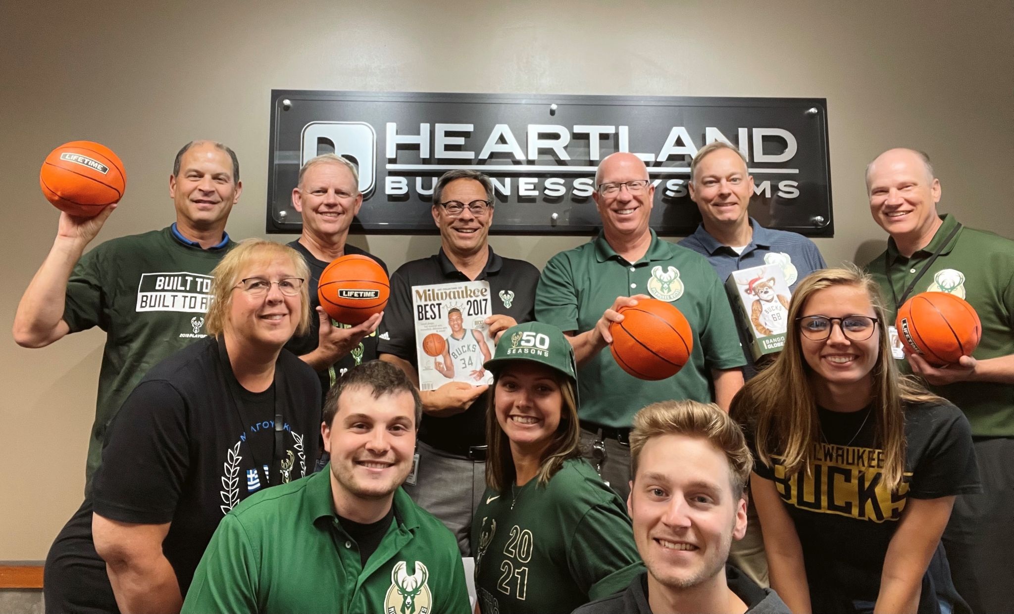 HBS employees in basketball shirts holding basketballs and memorabilia beneath the company sign