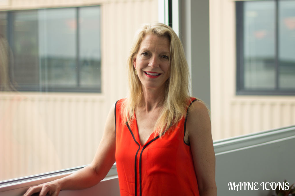 Heather Blease standing beside a window in a red dress, photographed for Maine Icons