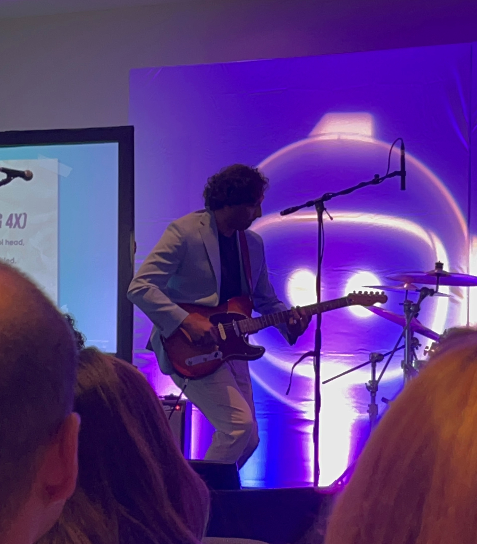 Hemanth Puttaswamy playing electric guitar on a purple-lit stage at a Malbek Envision event.