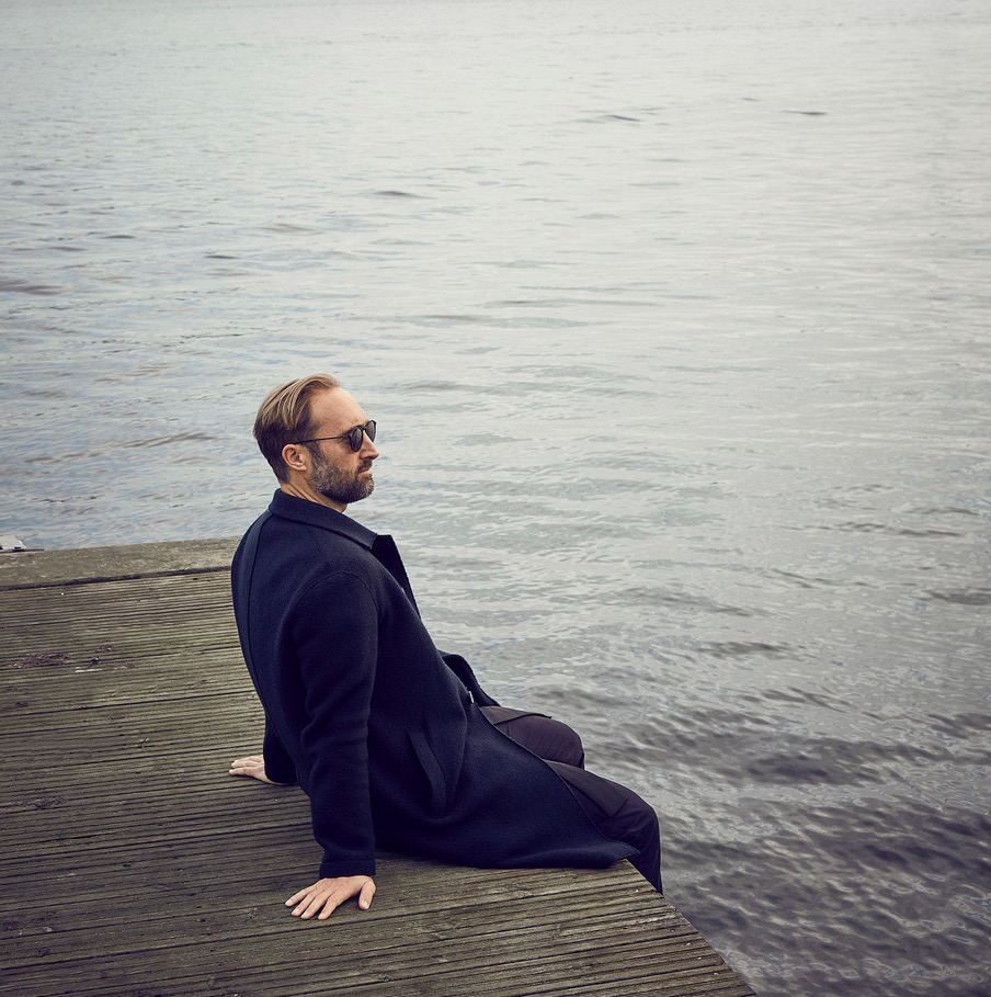 Henrik Zillmer wearing sunglasses and sitting beside the water on a wooden platform