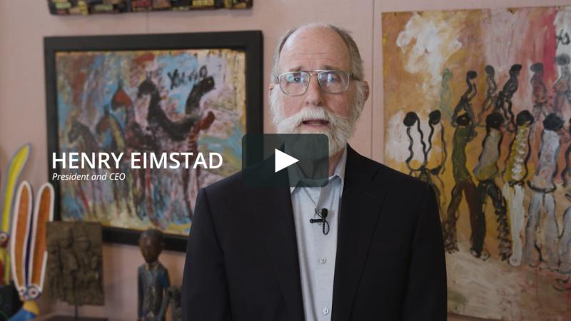 Henry Eimstad speaking in SIG’s 2023 welcome video, with colorful paintings behind him
