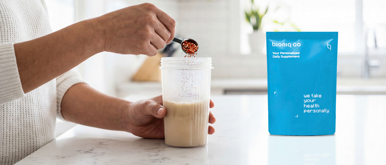Bioniq GO supplement granules being added to a prepared drink beside a blue product pouch
