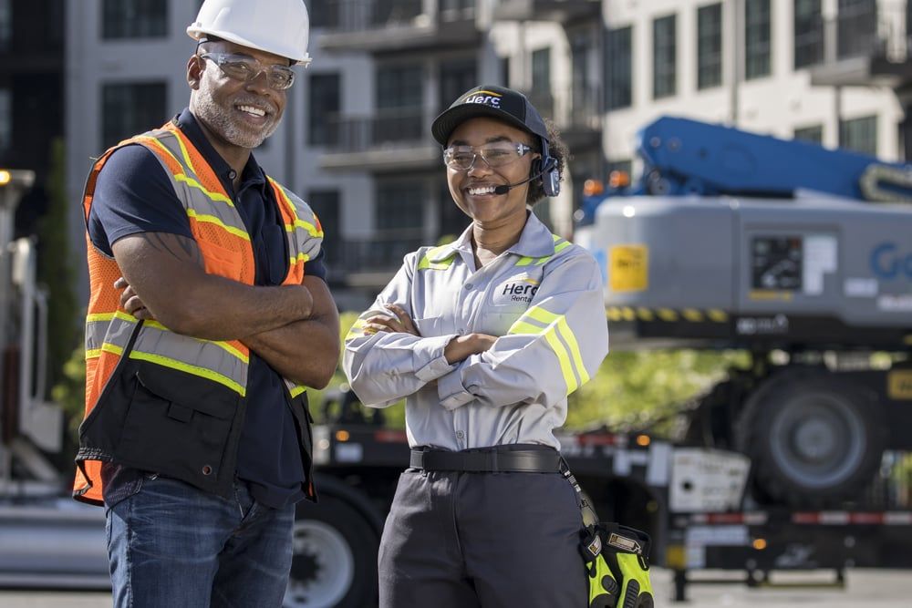 Two Herc team members wearing safety glasses beside a boom lift