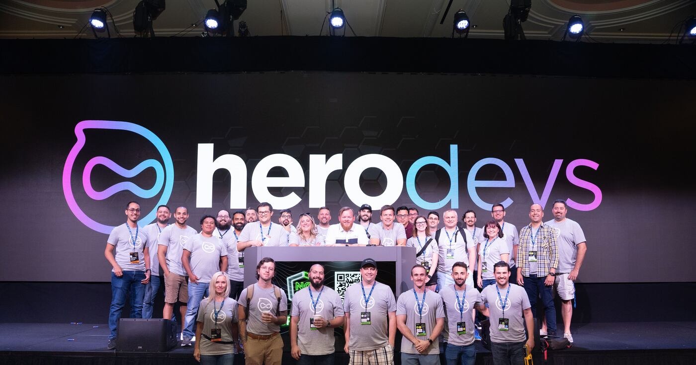 The HeroDevs team standing onstage beneath a large HeroDevs logo at ng-conf