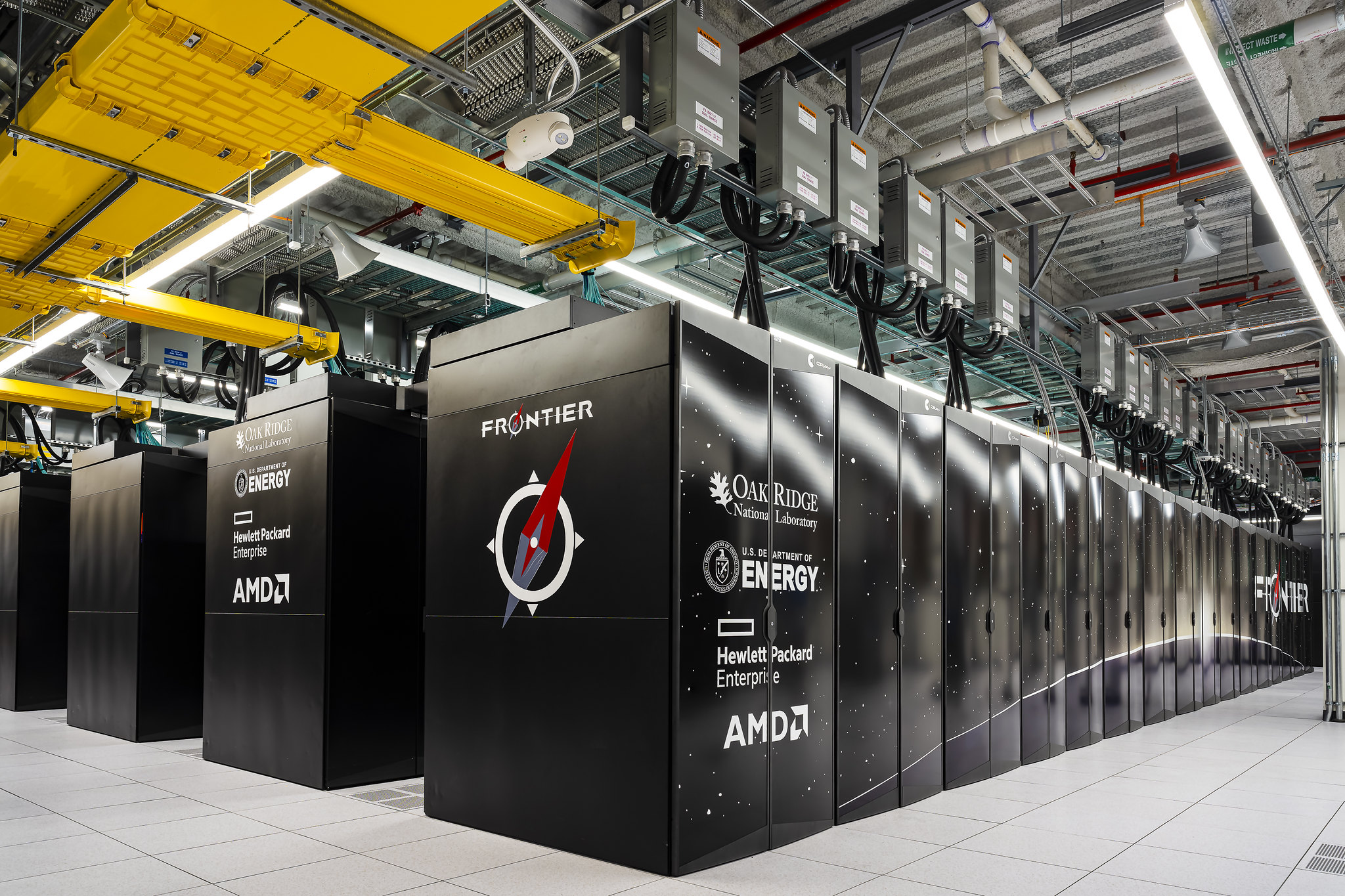 Rows of black HPE Cray Frontier cabinets beneath yellow cable trays at Oak Ridge National Laboratory