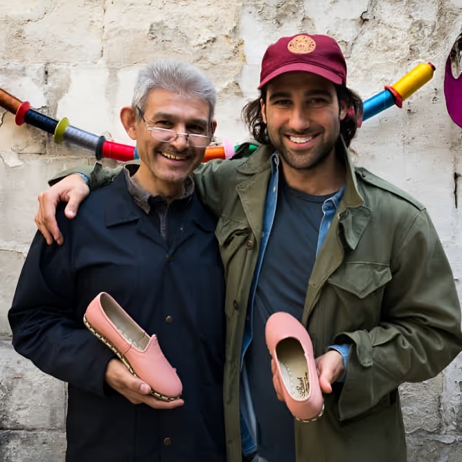 Two people holding pink Sabah shoes in a photograph published by Highbeam