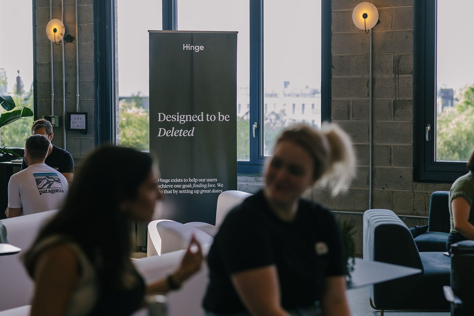 People talking at a Hinge gathering, with the company’s designed-to-be-deleted message behind them