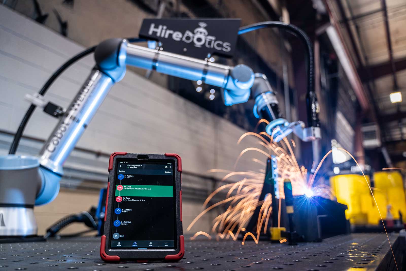 A Hirebotics collaborative robot welding beside a tablet running the Beacon app