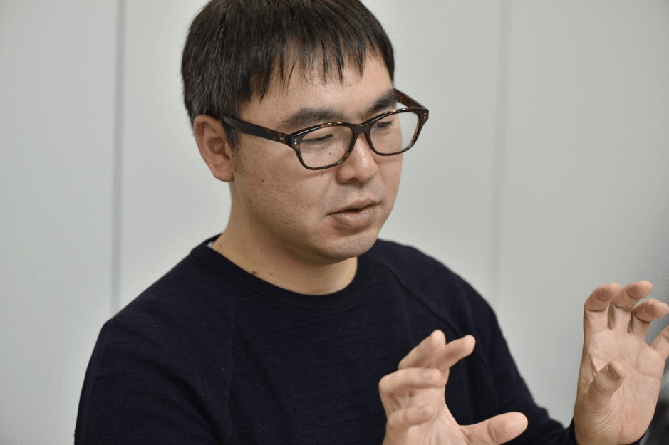 Hironobu Yoshikawa gesturing with both hands during his DIMENSION NOTE interview