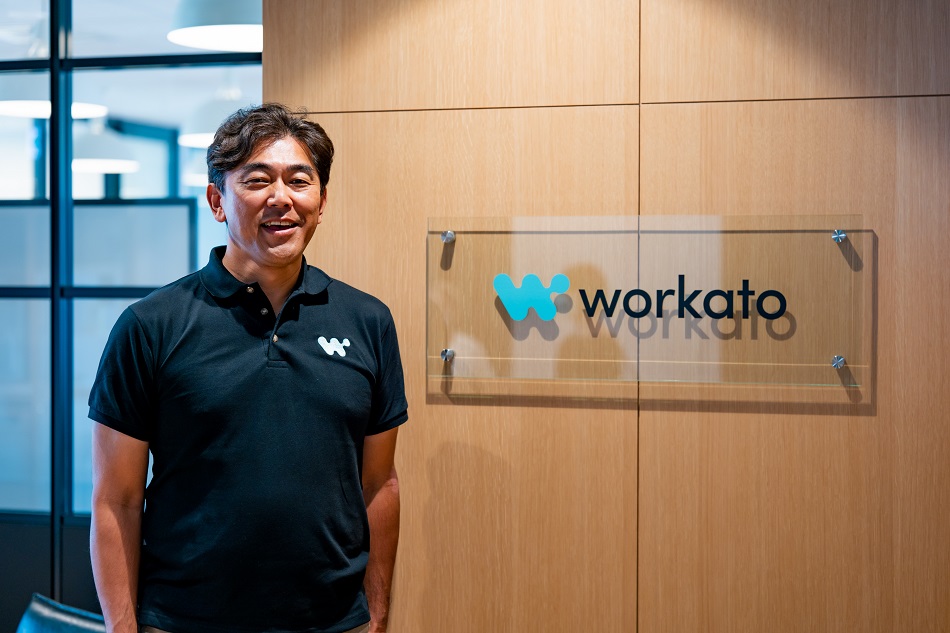 Hiroyuki Suzuki standing beside a Workato sign in an office