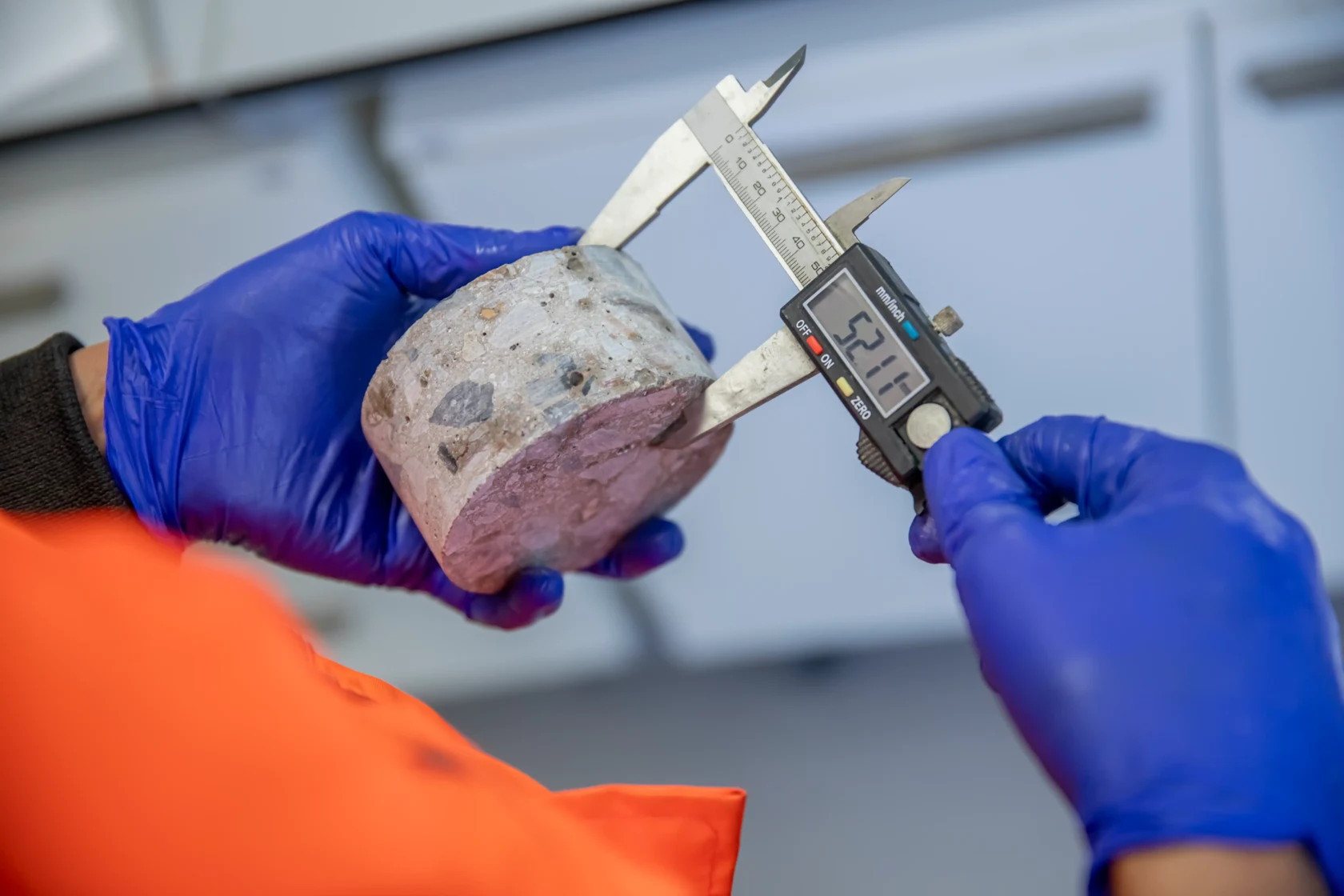 Gloved laboratory technician measures a cylindrical concrete specimen with a digital caliper