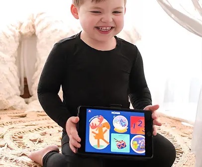 Smiling child holding a tablet displaying HOMER activities