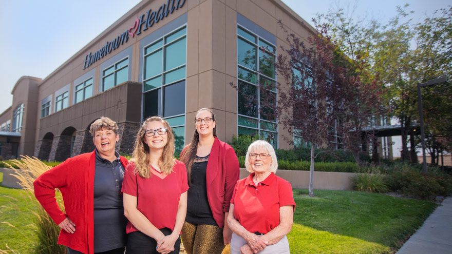 Four Hometown Health team members wearing red outside the company’s building