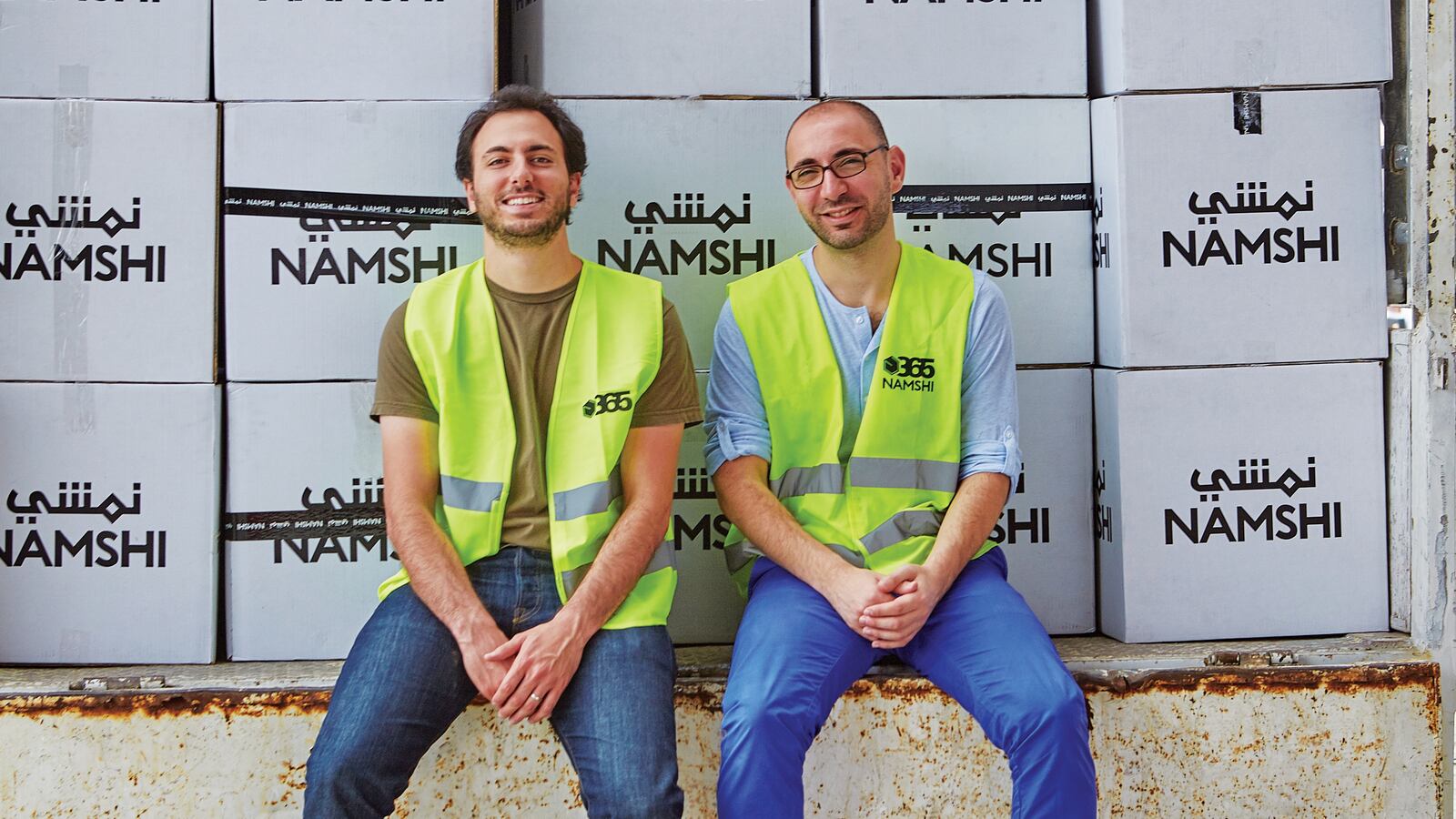 Namshi co-founders Hisham Zarka, left, and Hosam Arab, right, seated in high-visibility vests in front of stacked Namshi boxes