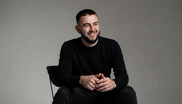 Hosanna founder Val Pavliuchenko seated and smiling in a black sweater
