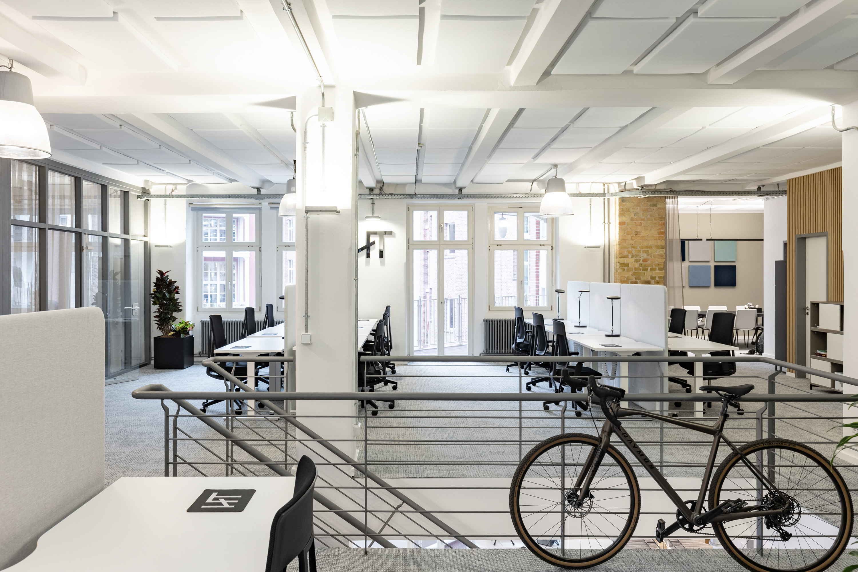 Bright HoFT Berlin campus workspace with shared desks, meeting areas and a bicycle beside the stair railing