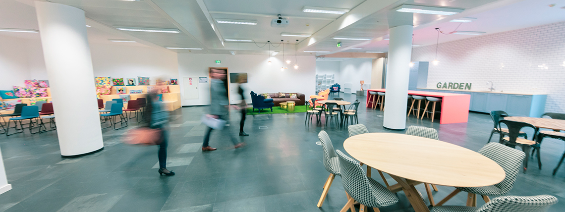 HoST shared event area with tables, colourful lounge seats and people moving through the space