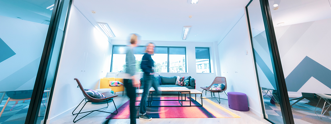 People walking through a bright HoST lounge with glass partitions and colourful seating