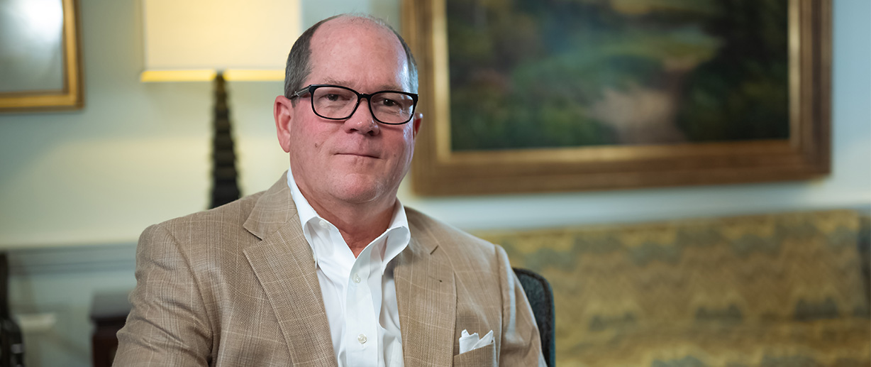 Howard Coker seated indoors, wearing glasses and a tan jacket