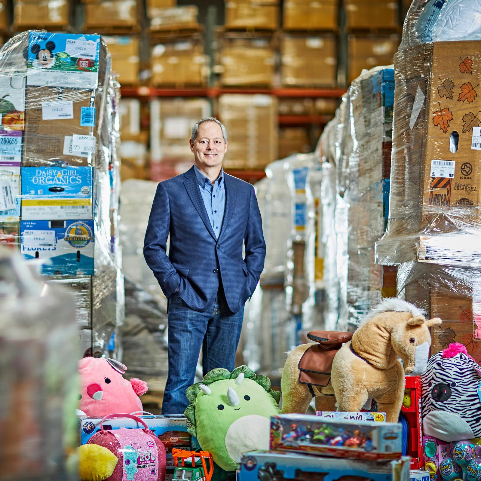 Howard Rosenberg standing among warehouse pallets and returned toys