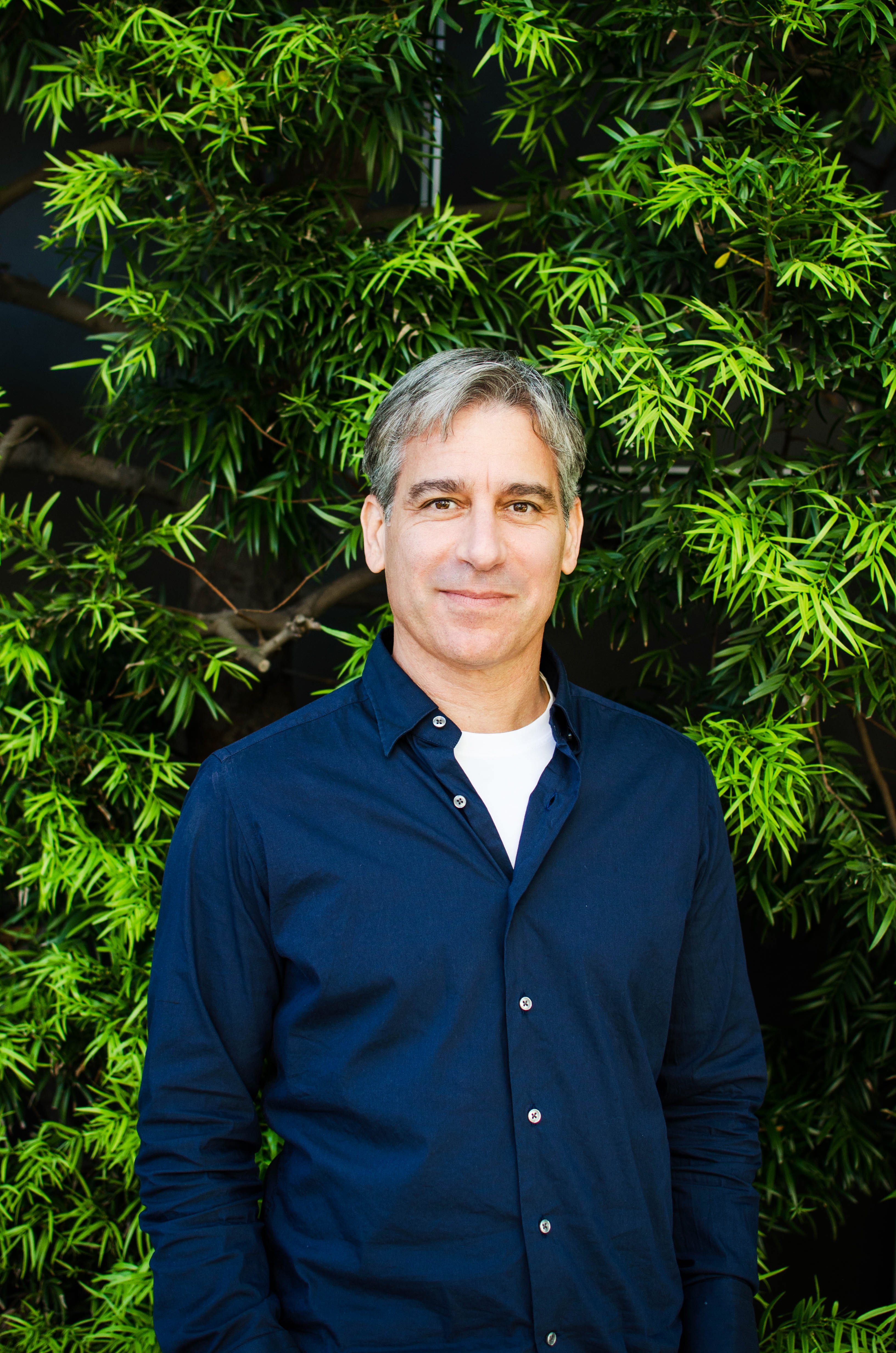 Howard Spector standing outdoors in a navy shirt, with green foliage behind him
