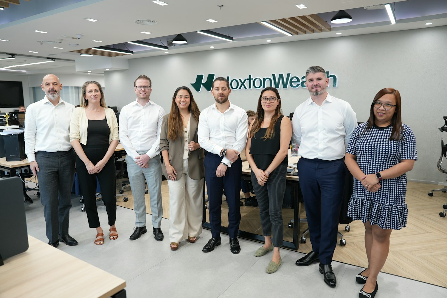 Eight members of the Hoxton Wealth team standing together in an office