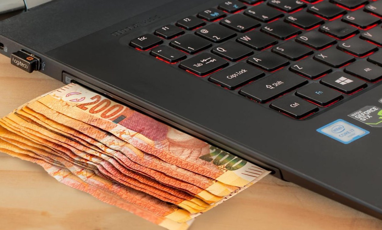 A laptop with paper currency tucked under the keyboard, illustrating money spent on marketing software.