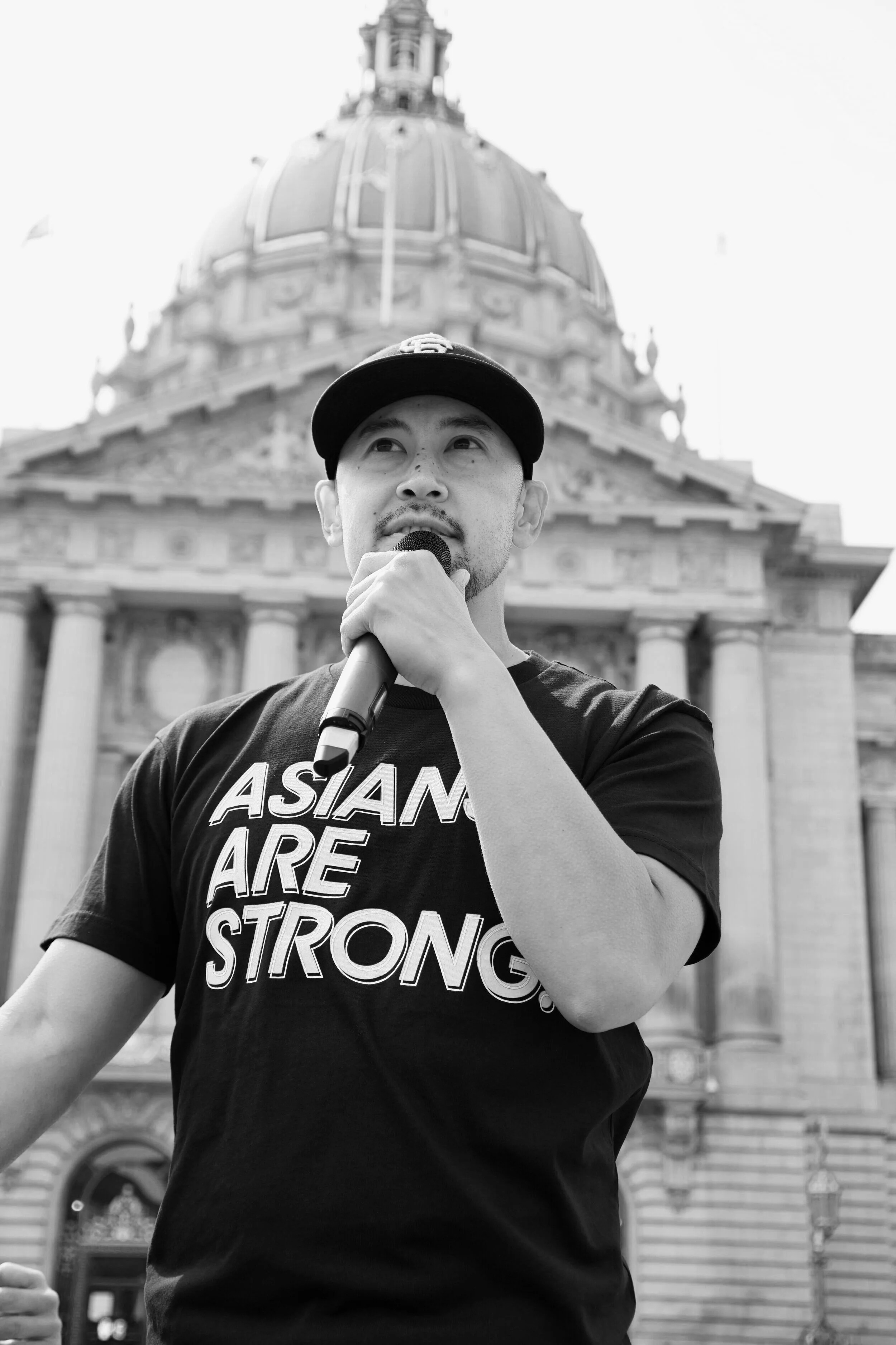 Hudson Liao speaking into a microphone outside San Francisco City Hall at an Asians Are Strong rally