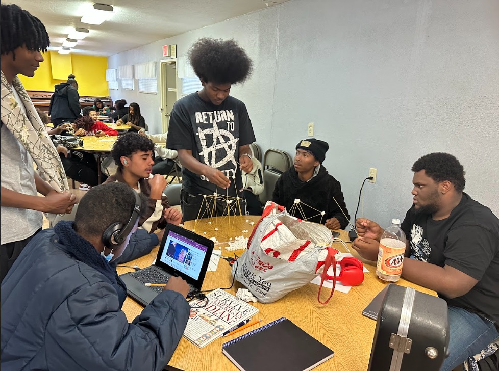 Young participants collaborating around laptops and project materials in a HumanBulb STEM workshop