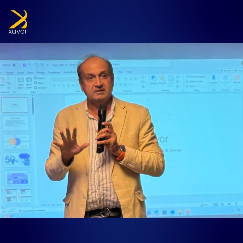 Hugh Rashid holding a microphone while addressing Xavor colleagues in front of projected presentation slides