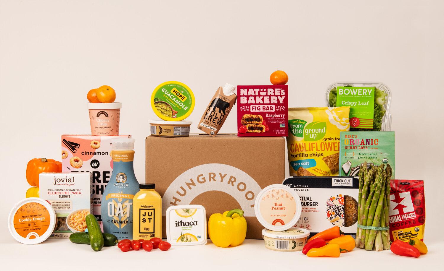 Hungryroot grocery box surrounded by vegetables, sauces, snacks, and packaged foods