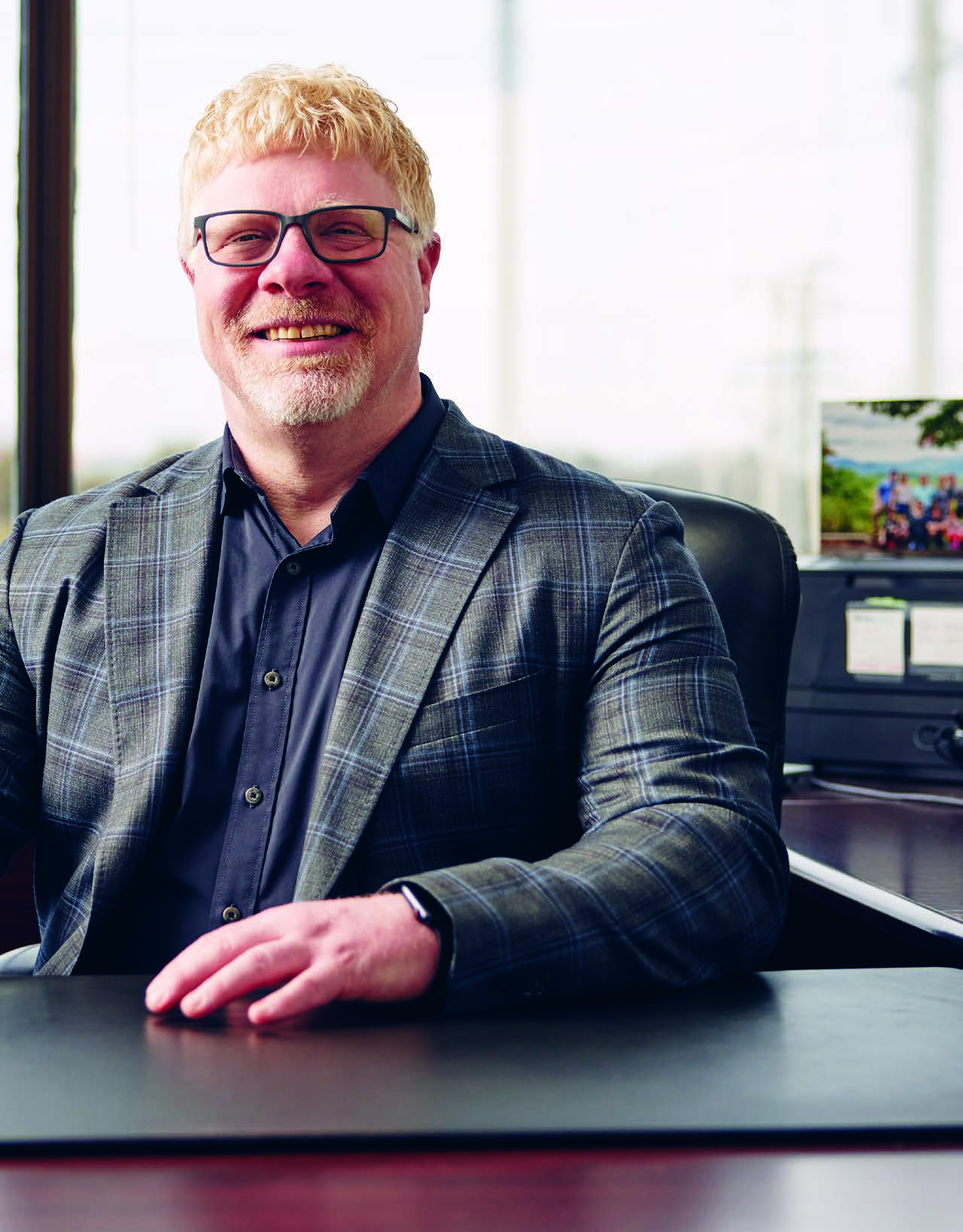 Ian Fredericks seated at his office desk, smiling in a checked jacket