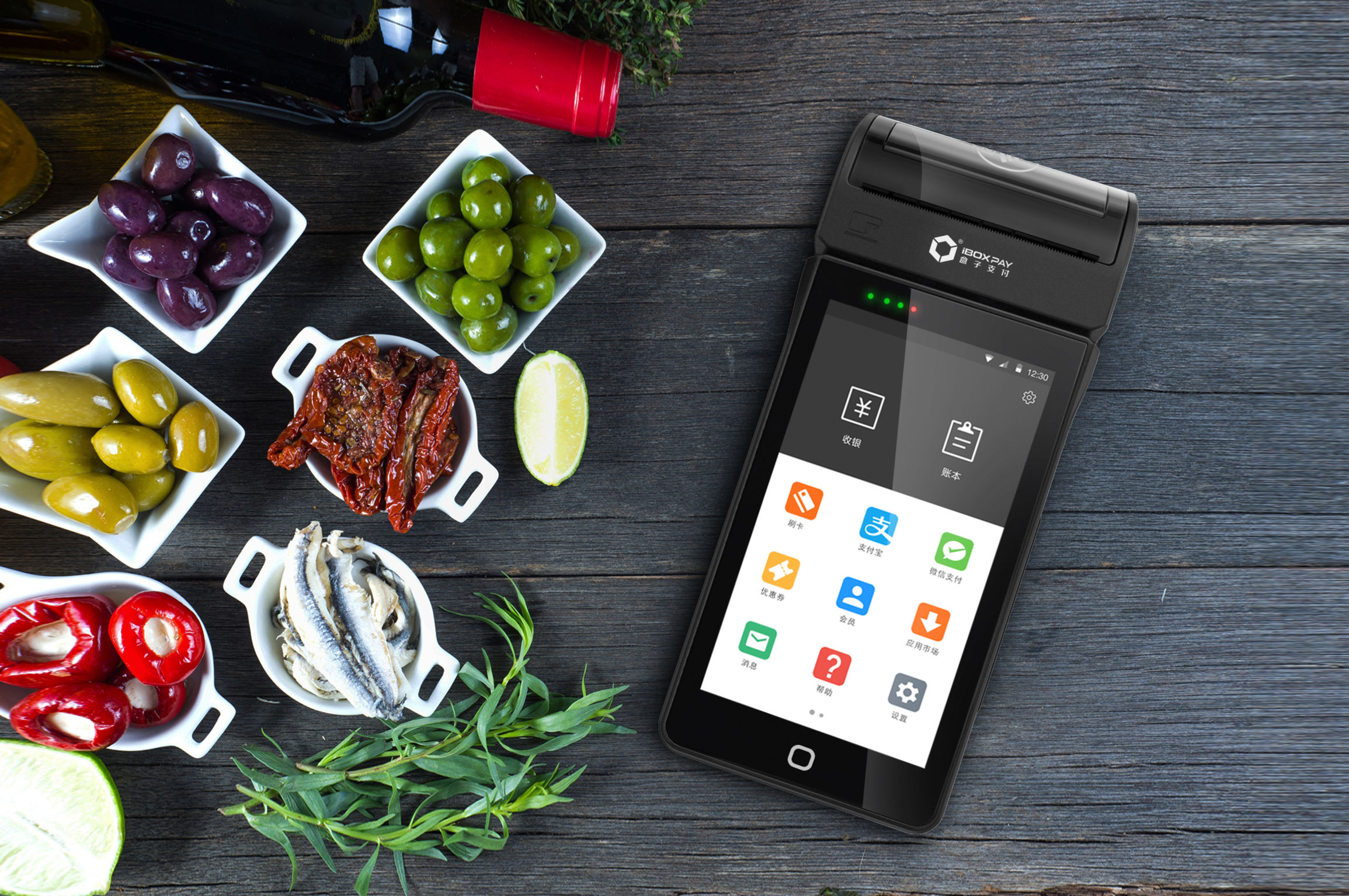 An iBoxPay S302 terminal on a wooden table surrounded by small dishes of olives and peppers